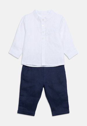 Chemise blanche à manches longues avec col mandarin, boutonnée, associée à un pantalon bleu marine à jambes droites pour enfant.