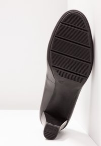 Semelle de cuir noir de chaussure à talons hauts, présentant des rainures horizontales pour la traction, avec un accent de talon effilé et un profile latéral légèrement courbé.