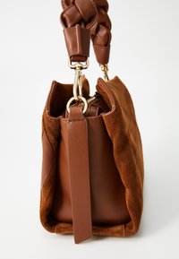 Brown suede and leather handbag with a braided handle, featuring gold-tone hardware and a soft, textured exterior. Zippered closure at top.