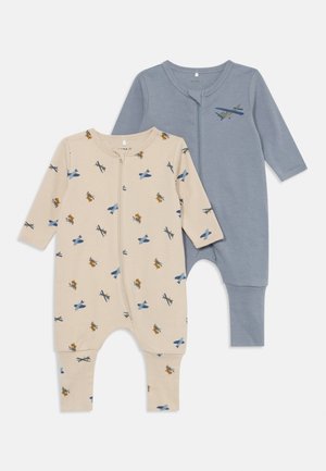 Dos monos para niños: uno beige con estampado de aviones, el otro azul sólido. Ambos tienen mangas largas, un cierre frontal y pantalones con pies.