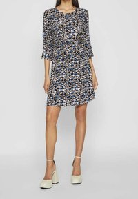 Robe fleurie avec des manches trois quarts, présentant un fond noir et un motif de fleurs bleues, blanches et beiges. Forme en A, tissu léger.