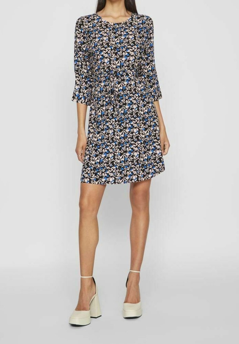 Robe fleurie avec des manches trois quarts, présentant un fond noir et un motif de fleurs bleues, blanches et beiges. Forme en A, tissu léger.