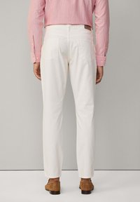 Pantalones de algodón blancos con un corte ajustado y dos bolsillos traseros, llevados con una camisa de rayas rosas y zapatos de ante marrón.