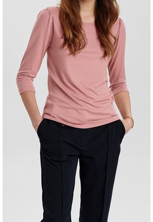 Rosa geripptes Langarmoberteil mit rundem Ausschnitt und gerafften Schultern, kombiniert mit dunkelblauen Hosen mit lockerem Schnitt.