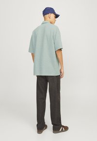 Lyseblå kortærmet polo skjorte med struktureret overflade, parret med mørke lige ben jeans og brune sneakers, set fra ryggen.
