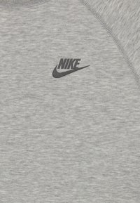 Grå atletisk tröja i ett texturerat tyg, med en svart Nike-logotyp på övre vänstra sidan. Rund halsringning och raglanärmar.