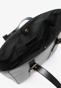 Black leather tote bag with a smooth exterior, gold hardware, and a fabric-lined interior. Includes an interior pocket for organization.
