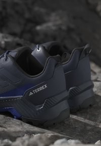Tmavomodré turistické topánky Adidas Terrex s odolnou podrážkou položené na kamenistom teréne v exteriéri.