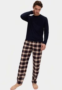 Top de manga larga en azul marino con cuello redondo, combinado con pantalones de pijama a cuadros en colores marrón, blanco y azul marino, con una cintura elástica.