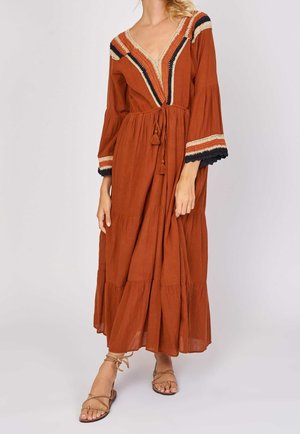 Rust-colored maxi dress with a deep V-neck, embroidered detailing, long sleeves, and a tiered skirt. Features decorative tassels and layered accents.