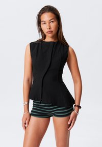 Top noir sans manches avec une finition texturée, présentant un ourlet courbé et une fermeture à un bouton à l'avant. Assorti à un short rayé.