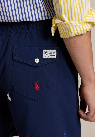 Κοντό παντελόνι ναυτικού στιλ με πίσω τσέπη που κλείνει με κουμπί, κεντητό λογότυπο αλόγου σε κόκκινο, μπλε και λευκό, και ετικέτα με εμπορικό σήμα.