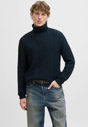Pull col roulé bleu marine avec un design en tricot torsadé texturé, manches longues et ourlet côtelé. Associé à un jean en denim délavé.