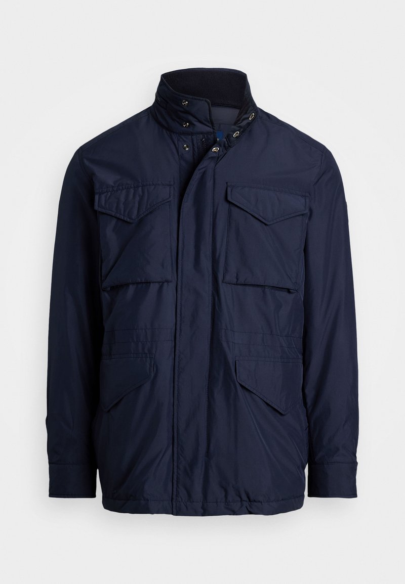 Tumši zila jaka, izgatavota no gludas auduma, ar divām krūšu kabatām, divām sānu kabatām un stāvu apkakli ar spiedpogu aizdari.