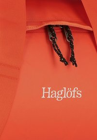 Borsa impermeabile rossa con parte superiore arrotondata, lacci neri regolabili e logo "Haglöfs" ricamato sul davanti.