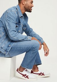 Lichtblauwe denimjack en bijpassende jeans. Witte sneakers met rode accenten. Glad textuur en nauwsluitende pasvorm. Eenvoudig, casual ontwerp.