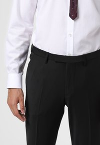 Schwarze Anzughose mit glatter Textur, mit Falten und tailliertem Bund, kombiniert mit einem frischen weißen Hemd und einer gepunkteten Krawatte.