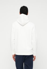 Λευκή κουκούλα με απαλή υφή, ριγωτούς καρπούς και ζώνη μέσης. Διαθέτει μια μεγάλη, κλασική κουκούλα και έναν καθαρό, μινιμαλιστικό σχεδιασμό.