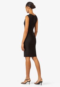 Schwarzes, tailliertes Kleid mit gerippter Textur, ärmellosem Design und einem Reißverschluss hinten in der Mitte. Kombiniert mit schwarzen, geschnürten Absatzsandalen.