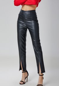 Pantalons en simili cuir noir taille haute avec une coupe ajustée, présentant des fentes sur les côtés à l'ourlet et une texture lisse pour un aspect élégant.