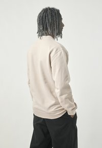 Light beige sweatshirt with long sleeves and a relaxed fit, featuring a round neck and soft texture, worn with black pants.