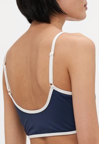Marineblå bikini topp med hvit kant, med justerbare stropper og en jevn tekstur, designet for en tettsittende passform.