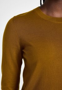 Senapsgul stickad tröja med rund halsringning och långa ärmar. Texturen är slät med ett fint ribbat mönster.
