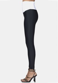 Leggings neri con una vita alta bianca, caratterizzati da una texture liscia e una silhouette aderente; indossati con sandali con tacco a spillo neri.