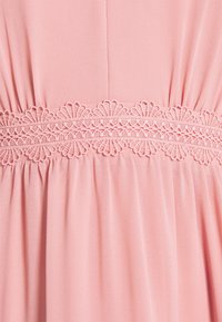 Różowa tkanina sukienki o marszczonej strukturze oraz szczegółowym koronkowym wykończeniu wzdłuż talii, z kwiatowymi wzorami w kontrastowym odcieniu.