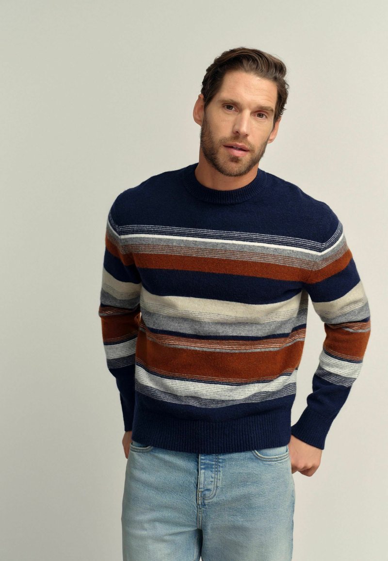 Navy blue knit sweater with horizontal stripes in shades of rust, gray, and cream. Features a ribbed neckline and cuffs, and a relaxed fit.