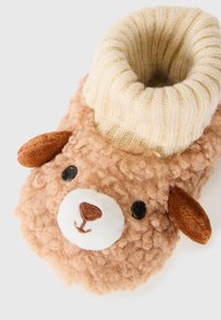 Myke brune babysokker med et teddy-bjørn-ansikt og kremfarget ribbestrikket mansjett på hvit bakgrunn.