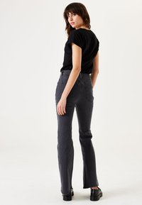 Zwart kortemouwen t-shirt gecombineerd met hoog-getailleerde, donkergrijze flared jeans. De jeans hebben twee achterzakken en een gladde textuur. Zwarte schoenen.