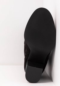 Czarny zamszowy but z gładkim, lekko zaostrzonym noskiem i płaską, gumową podeszwą z teksturowanym bieżnikiem. Obcas jest minimalistyczny i szeroki.