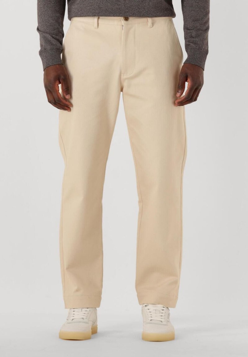 Bež krojene hlače ravnog kroja, izrađene od glatkog materijala, s prednjim zatvaračem i kopčanjem na dugme, uparenim s bijelim tenisicama.