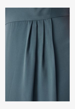 Un abito drappeggiato in un colore verde teal tenue, con tessuto morbido e plissettato, dalla texture liscia e cuciture ridotte al minimo.