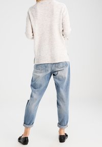 Lichtgrijze gebreide trui met opgerolde mouwen, gecombineerd met lichtblauwe relaxte jeans, opgerold bij de enkels, en zwarte platte schoenen.