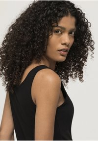 Top nero senza maniche dal design aderente, realizzato in tessuto morbido e con una texture liscia, abbinato a capelli ricci che incorniciano il viso.