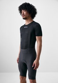 Der schwarze Radsportanzug verfügt über einen oberen Abschnitt aus Netzgewebe mit kurzen Ärmeln und elastischen Trägern, kombiniert mit figurbetonten Shorts und einem gepolsterten Sitzbereich.