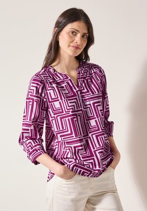 Blouse à manches longues en violet avec un motif géométrique. Présente un col en V avec de légers fronces et des manches retroussées. Fabriquée en tissu léger.