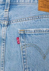 Poche arrière d'un jean denim bleu clair avec une étiquette rouge Levi's et un patch de marque en cuir marron montrant les détails des coutures.