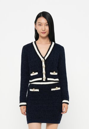 Abito di maglia blu navy con bordi bianchi, scollatura a V, maniche lunghe e dettagli in bottone dorato su tasche e parte frontale, caratterizzato da un design testurizzato.