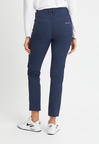Marinblå tights med en åtsittande design, två bakfickor och synliga sömmar. Bärs tillsammans med vita och svarta Nike-sneakers.