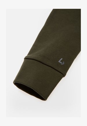 Ciemnozielona bawełniana koszula z długim rękawem, mankiet z ribbowanym wzorem i małym szarym logo przy otworze rękawa. Czysty, minimalistyczny design.