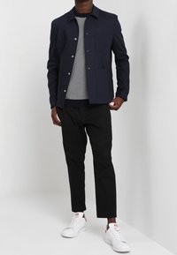 Giacca navy con tasche frontali, camicia a righe bianche e navy, pantaloni neri e sneakers bianche con accenti rossi. Tessuto morbido, vestibilità moderna.