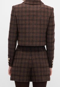 Afkortet brun ternet blazer med tekstureret stof, med krave og manchetter med guldknapper, kombineret med matchende shorts.