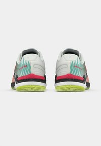 Par sportske cipele u raznolikim bojama s zelenim potplatom, crnim i crvenim detaljima, prikazane s leđa na bijeloj pozadini.