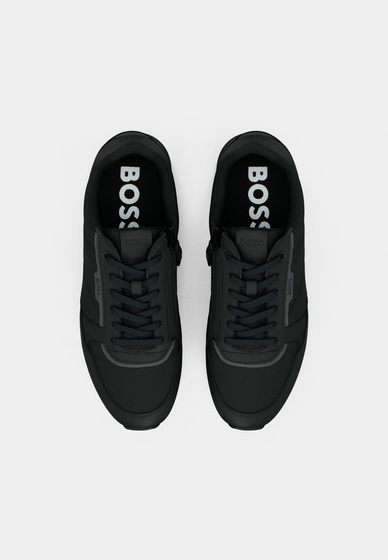 Une paire de baskets noires BOSS avec des lacets, des zips sur les côtés et un logo sur la languette, les côtés et les semelles intérieures, vue de dessus sur un fond blanc.