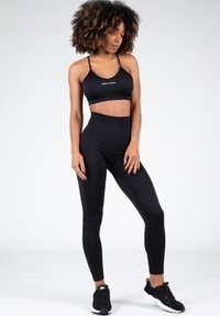  Sujetador deportivo negro y leggings de tiro alto hechos de material elástico. Usados con zapatillas negras, que presentan un diseño minimalista y una marca sutil.