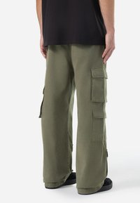 Pantaloni cargo din țesătură verde măsliniu au o croială lejeră, două buzunare laterale mari și cusături întărite. Purtați cu pantofi negri.