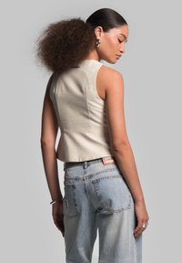 Helles beige, kurzes Tanktop aus strukturiertem Stoff, kombiniert mit hellblauen, hoch taillierten Jeans mit Gesäßtaschen und einem orangen Logoetikett.